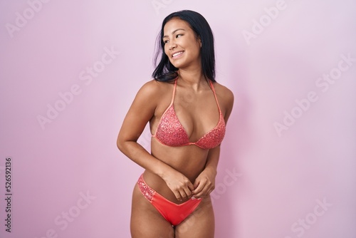 Hispanic woman wearing bikini looking away to side with smile on face, natural expression. laughing confident.