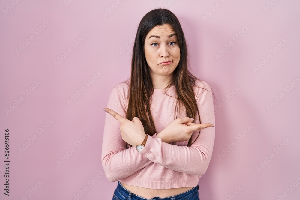 Fototapeta premium Young brunette woman standing over pink background pointing to both sides with fingers, different direction disagree