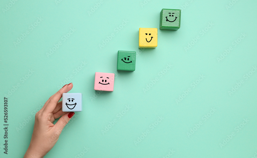 Female hand and colorful cubes with different drawn emoticons on turquoise background Female hand and colorful cubes with different drawn emoticons on turquoise background