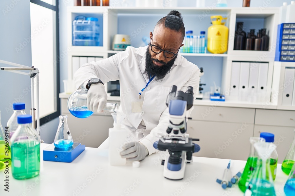 Young african american man wearing scientist uniform measuring liquid at laboratory Young african american man wearing scientist uniform measuring liquid at laboratory