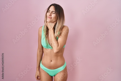 Young hispanic woman wearing bikini over pink background touching painful neck, sore throat for flu, clod and infection
