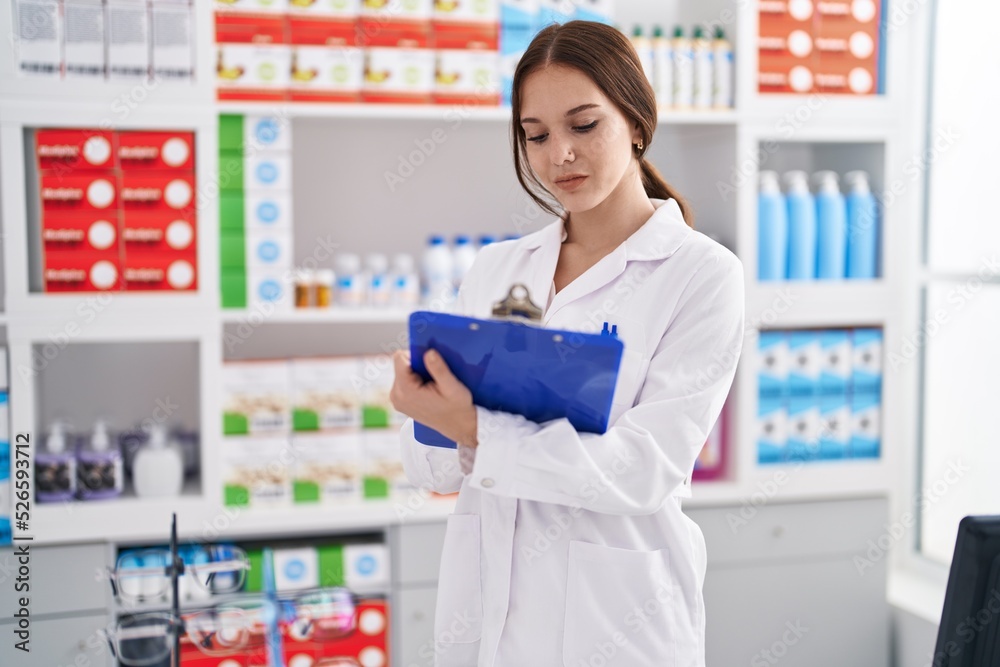 Young woman pharmacist writing on clipboard at pharmacy