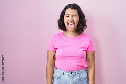 Young hispanic woman standing over pink background sticking tongue out happy with funny expression. emotion concept.