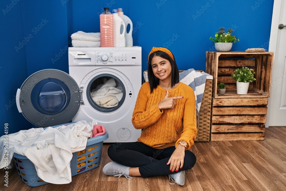 Young hispanic woman doing laundry cheerful with a smile on face pointing with hand and finger up to the side with happy and natural expression Young hispanic woman doing laundry cheerful with a smile on face pointing with hand and finger up to the side with happy and natural expression