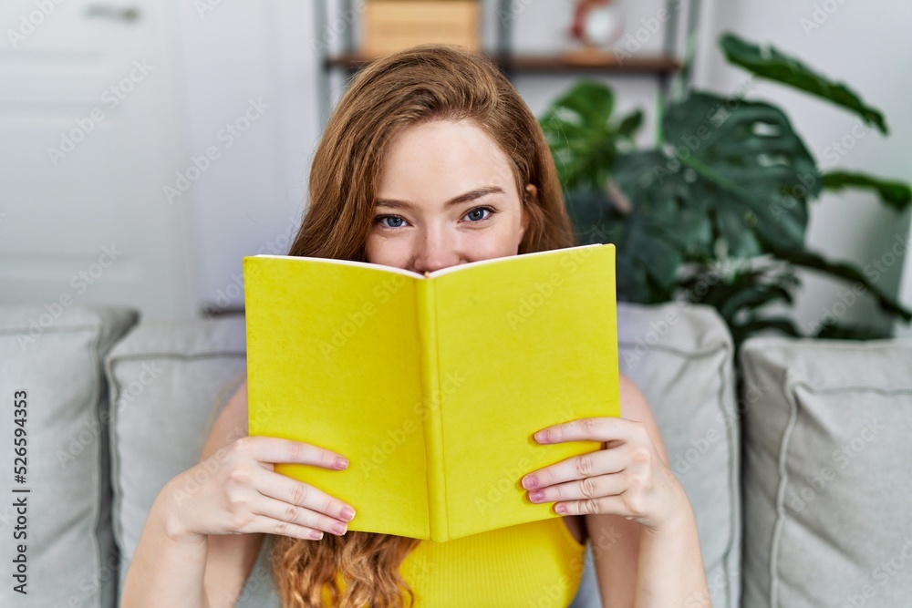 Young redhead girl smiling happy covering face with book at home Young redhead girl smiling happy covering face with book at home