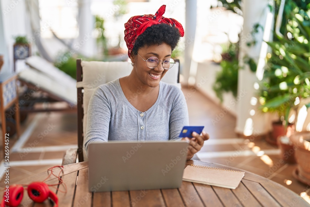 African american woman using laptop and credit card sitting on table at home terrace