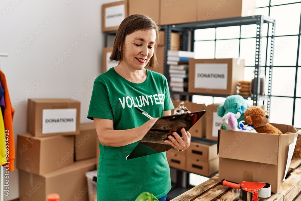 Middle age hispanic woman checking donations on checklist at donations stand