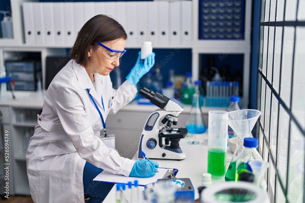 Middle age woman scientist holding pills at laboratory Middle age woman scientist holding pills at laboratory