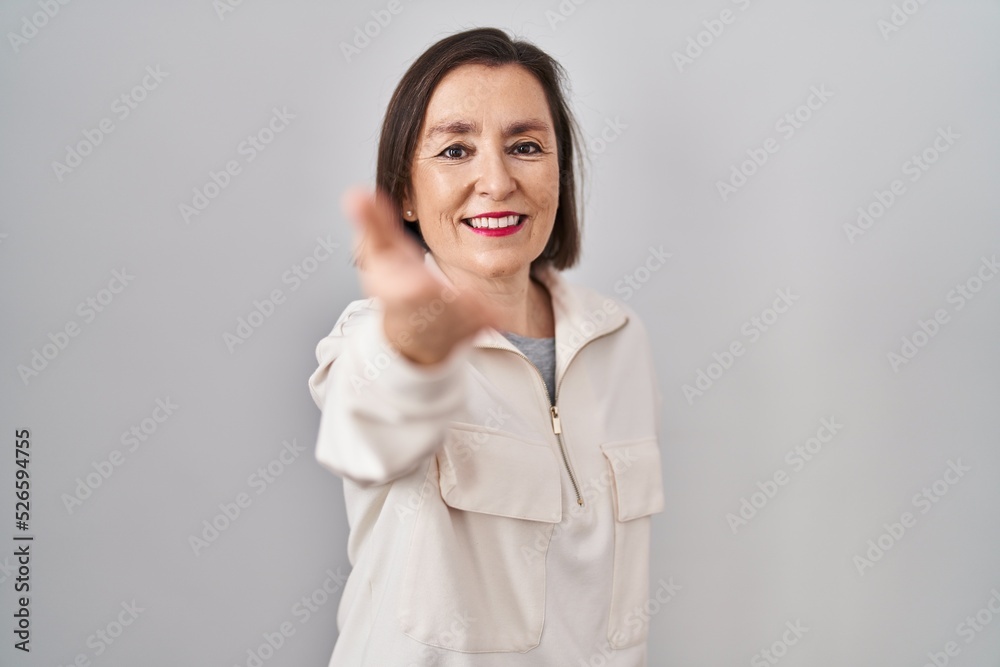 Middle age hispanic woman standing over isolated background smiling cheerful offering palm hand giving assistance and acceptance. Middle age hispanic woman standing over isolated background smiling cheerful offering palm hand giving assistance and acceptance.