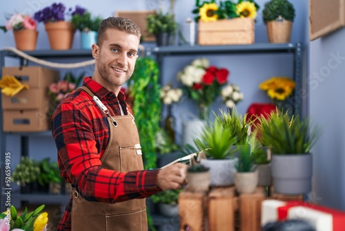 Young caucasian man florist smiling confident using laptop at flower shop