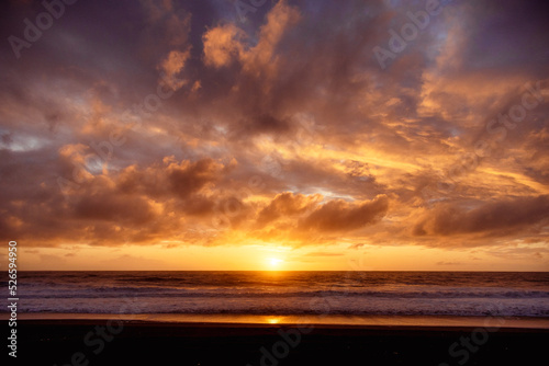 Paisaje de atardecer en la playa con ocaso en el mar y nubes iluminadas por el sol © Richard