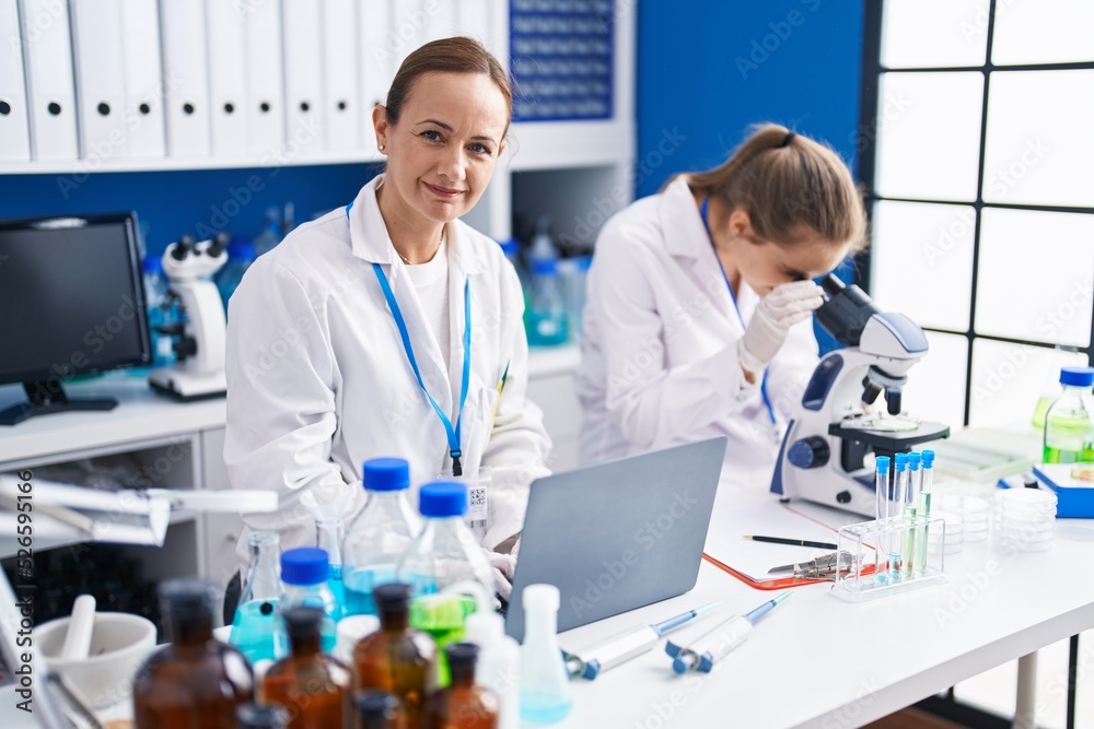 Two women scientists using microscope and laptop at laboratory Two women scientists using microscope and laptop at laboratory