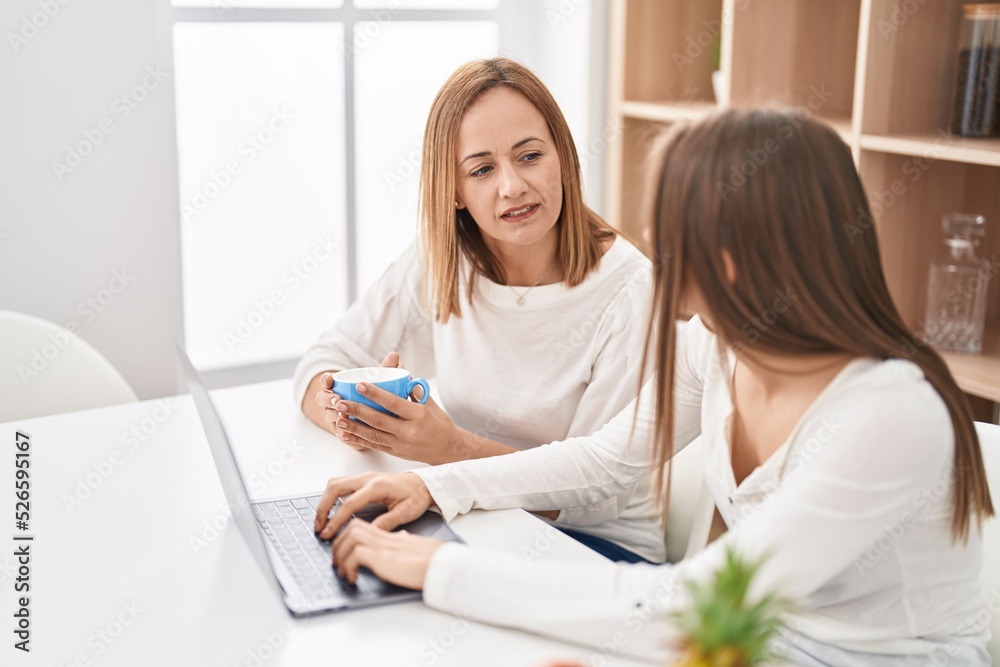 Two women mother and daughter using laptop drinking coffee at home Two women mother and daughter using laptop drinking coffee at home