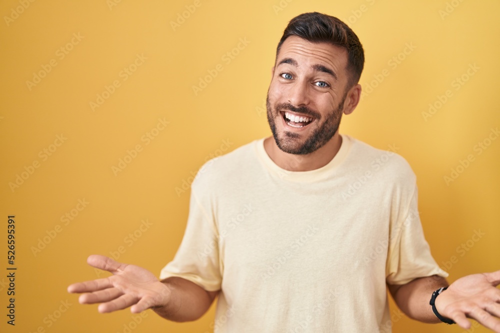 Handsome hispanic man standing over yellow background smiling cheerful with open arms as friendly welcome, positive and confident greetings Handsome hispanic man standing over yellow background smiling cheerful with open arms as friendly welcome, positive and confident greetings