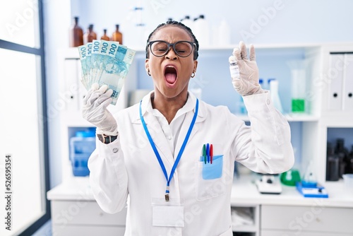 African woman with braids working at scientist laboratory holding money angry and mad screaming frustrated and furious  shouting with anger looking up.