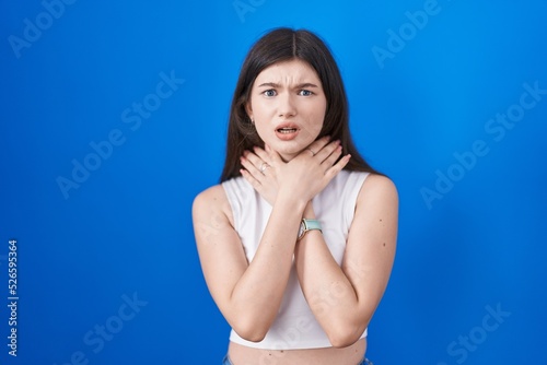 Young caucasian woman standing over blue background shouting suffocate because painful strangle. health problem. asphyxiate and suicide concept.
