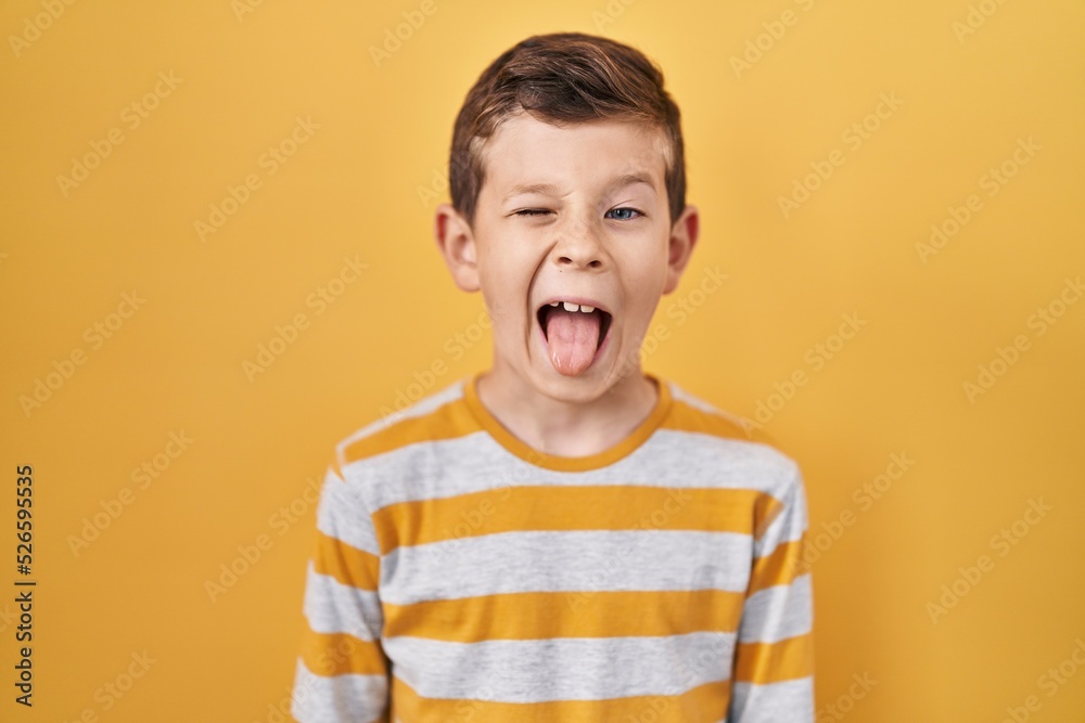 Young caucasian kid standing over yellow background sticking tongue out happy with funny expression. emotion concept. Young caucasian kid standing over yellow background sticking tongue out happy with funny expression. emotion concept.