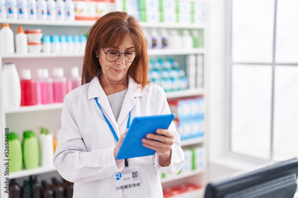 Middle age woman pharmacist using touchpad working at pharmacy