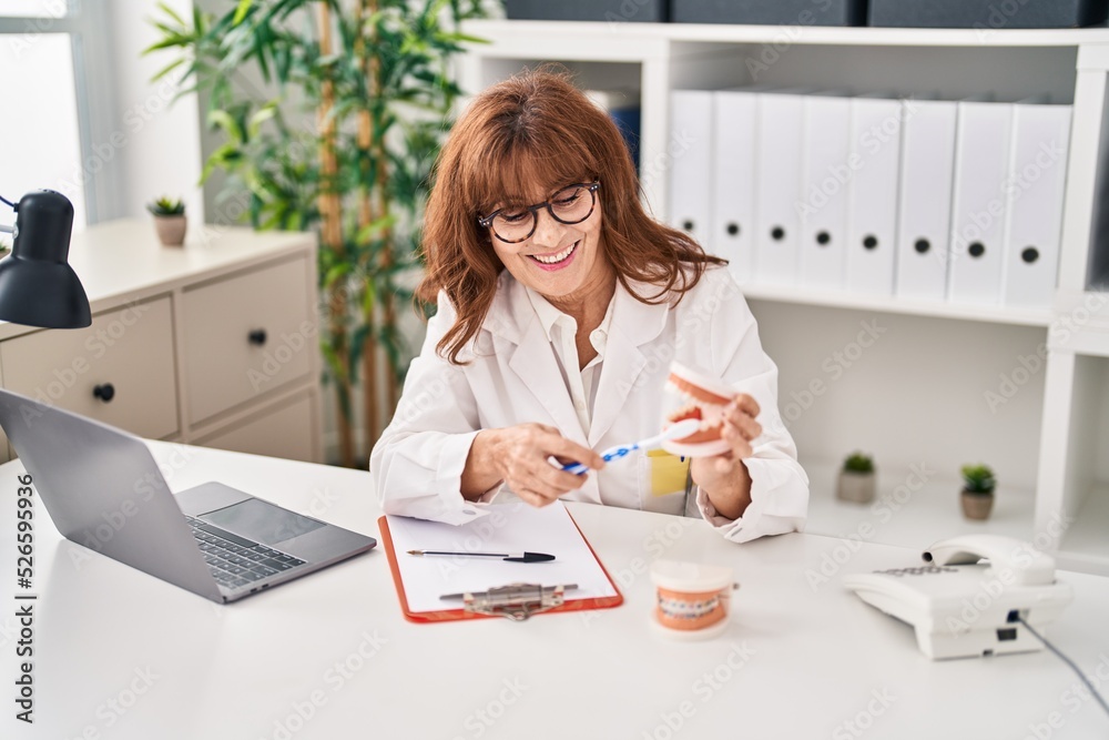 Middle age woman wearing dentist uniform teaching to clean teeth at clinic Middle age woman wearing dentist uniform teaching to clean teeth at clinic