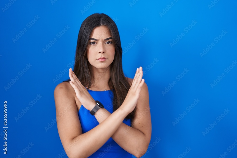 Hispanic woman standing over blue background rejection expression crossing arms doing negative sign, angry face Hispanic woman standing over blue background rejection expression crossing arms doing negative sign, angry face