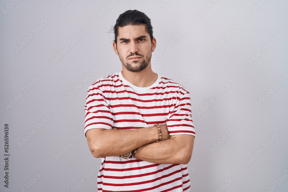Hispanic man with long hair standing over isolated background skeptic and nervous, disapproving expression on face with crossed arms. negative person. Hispanic man with long hair standing over isolated background skeptic and nervous, disapproving expression on face with crossed arms. negative person.
