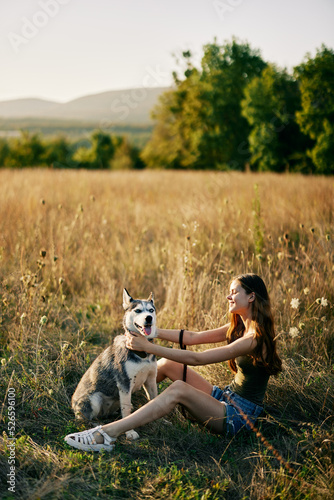 Woman sitting in field with dachshund dog smiling while spending time in nature with friend dog in autumn at sunset while traveling