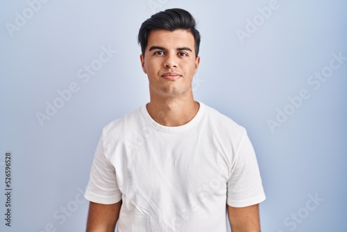 Hispanic man standing over blue background relaxed with serious expression on face. simple and natural looking at the camera.