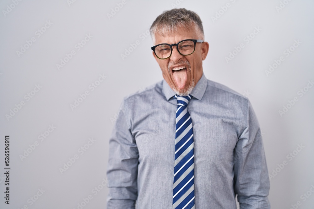 Hispanic business man with grey hair wearing glasses sticking tongue out happy with funny expression. emotion concept. Hispanic business man with grey hair wearing glasses sticking tongue out happy with funny expression. emotion concept.