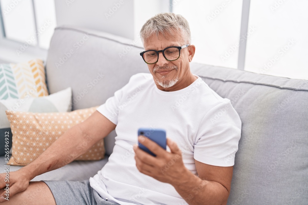 Middle age grey-haired man using smartphone sitting on sofa at home Middle age grey-haired man using smartphone sitting on sofa at home