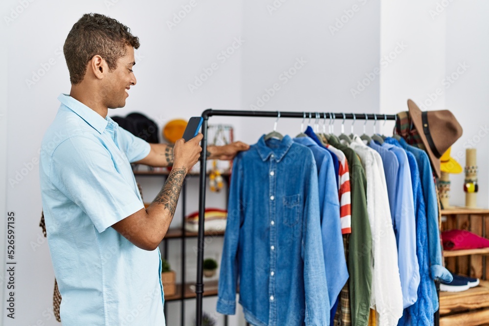 Young hispanic man shopping taking pictures to clothes at retail shop Young hispanic man shopping taking pictures to clothes at retail shop