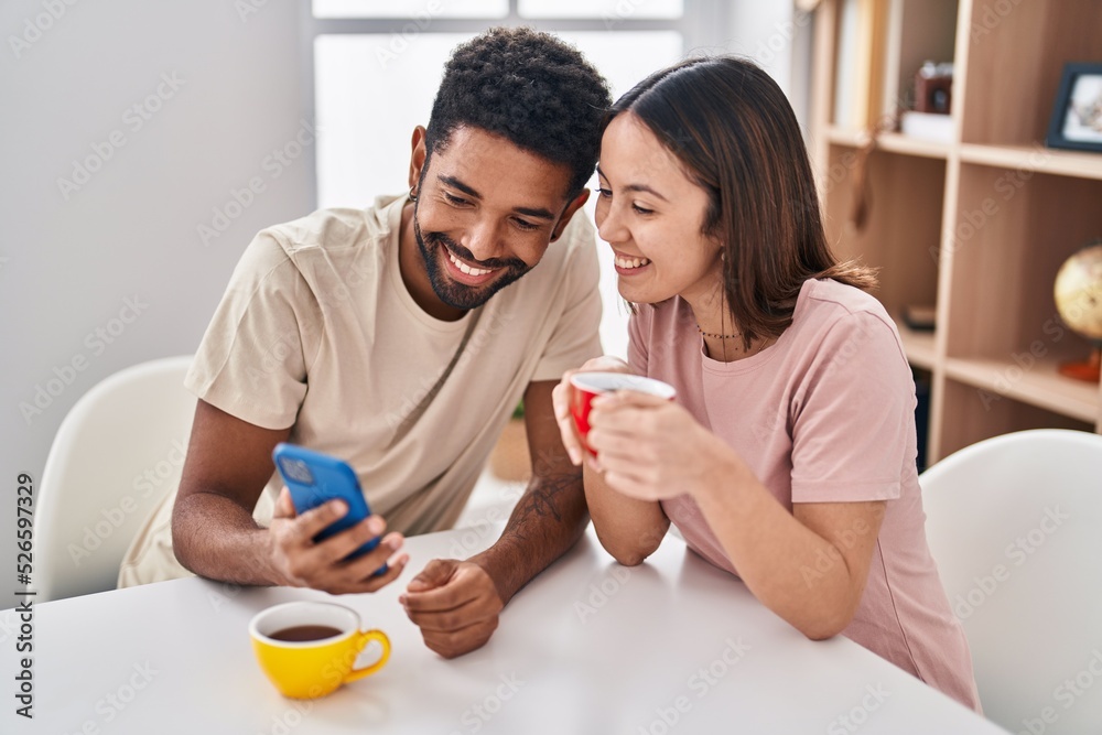 Man and woman couple sitting on table drinking coffee using smartphone at home