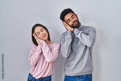 Young hispanic couple standing together sleeping tired dreaming and posing with hands together while smiling with closed eyes.