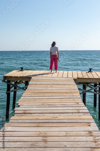 Young woman in pink pants watching the mediterranean sea on a wooden walkway, Palma de Mallorca
