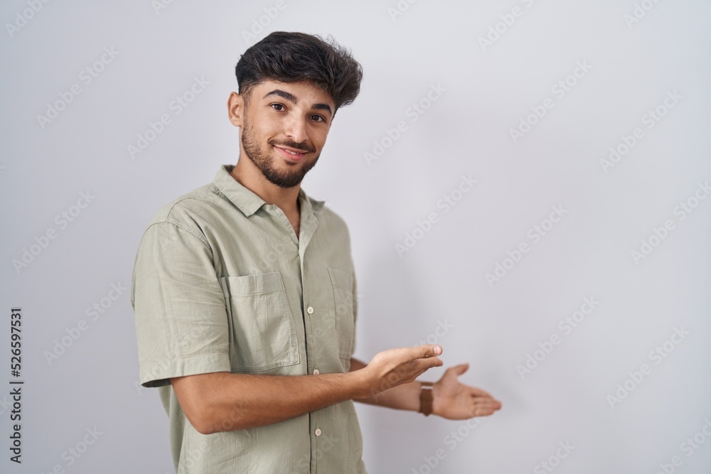Arab man with beard standing over white background inviting to enter smiling natural with open hand Arab man with beard standing over white background inviting to enter smiling natural with open hand