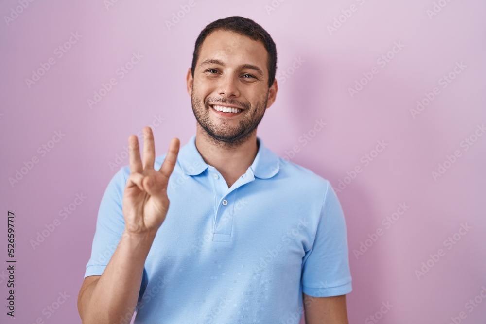 Hispanic man standing over pink background showing and pointing up with fingers number three while smiling confident and happy. Hispanic man standing over pink background showing and pointing up with fingers number three while smiling confident and happy.