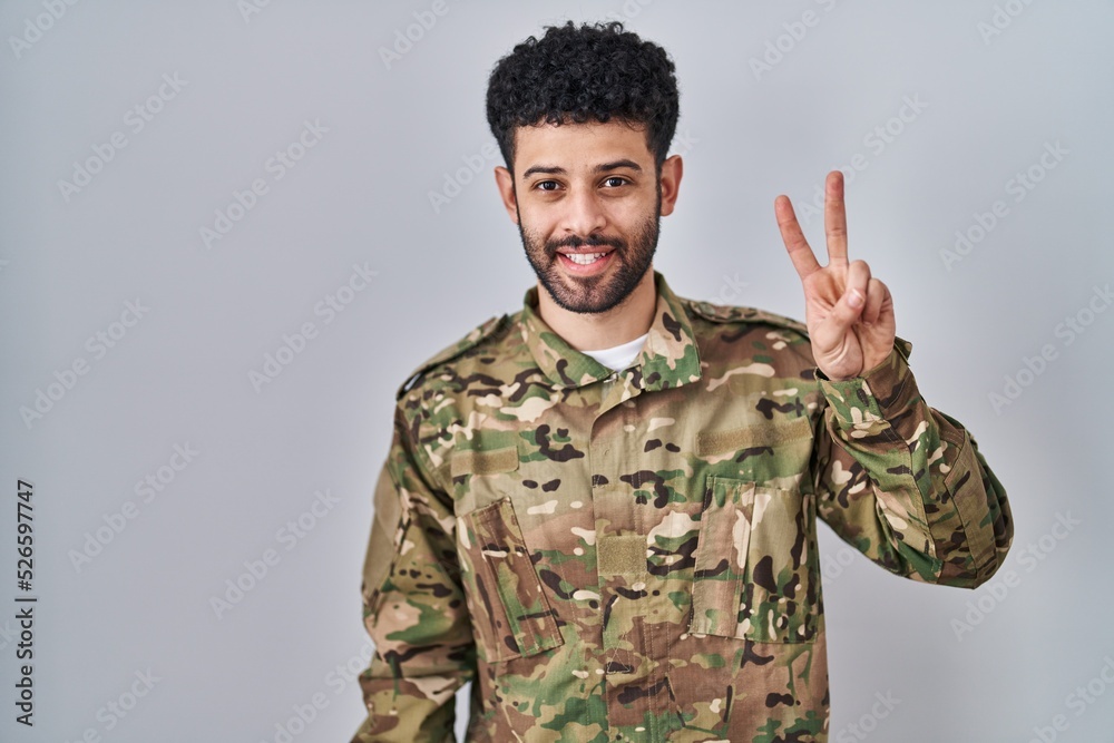Arab man wearing camouflage army uniform showing and pointing up with fingers number two while smiling confident and happy. Arab man wearing camouflage army uniform showing and pointing up with fingers number two while smiling confident and happy.
