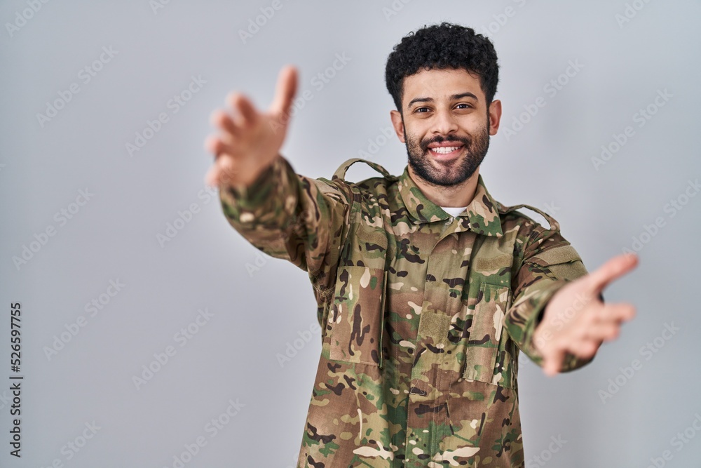 Arab man wearing camouflage army uniform looking at the camera smiling with open arms for hug. cheerful expression embracing happiness. Arab man wearing camouflage army uniform looking at the camera smiling with open arms for hug. cheerful expression embracing happiness.