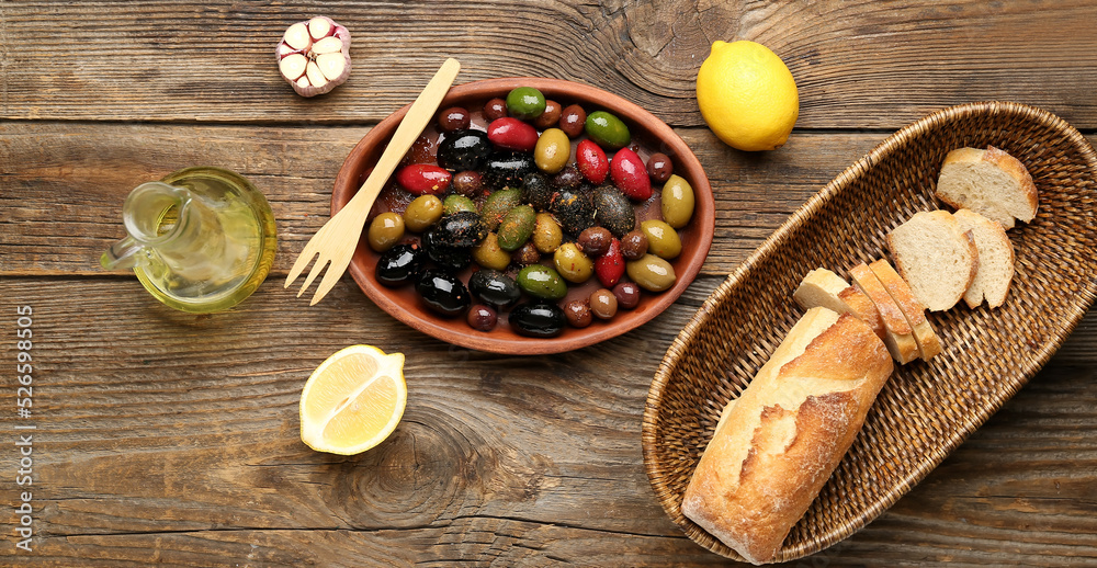 Composition with plate of delicious olives and bread on wooden background