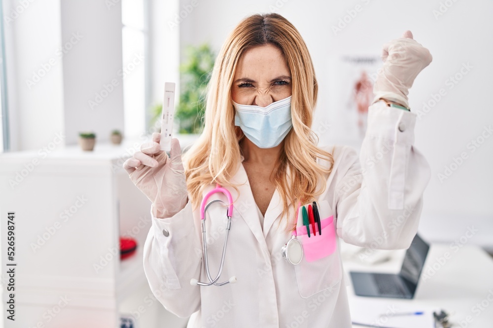 Young caucasian doctor woman holding covid test annoyed and frustrated shouting with anger, yelling crazy with anger and hand raised Young caucasian doctor woman holding covid test annoyed and frustrated shouting with anger, yelling crazy with anger and hand raised