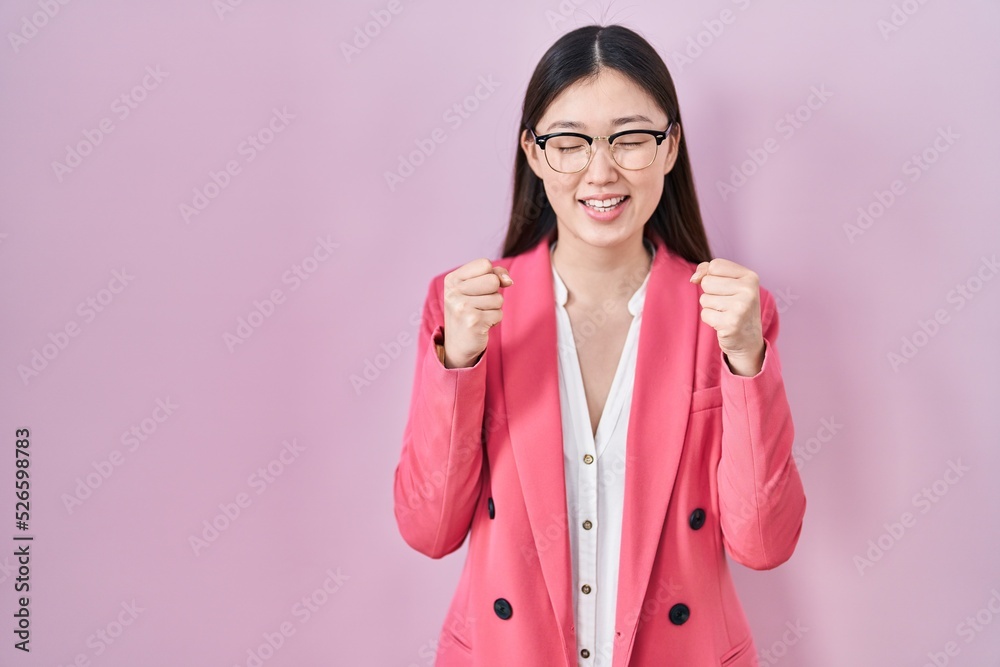 Chinese business young woman wearing glasses excited for success with arms raised and eyes closed celebrating victory smiling. winner concept. Chinese business young woman wearing glasses excited for success with arms raised and eyes closed celebrating victory smiling. winner concept.