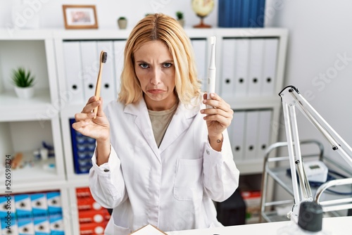 Beautiful blonde dentist woman holding electric toothbrush and normal toothbrush depressed and worry for distress, crying angry and afraid. sad expression.