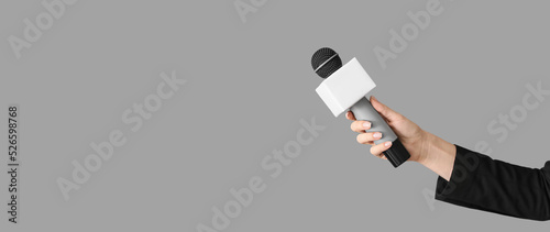Journalist's hand holding microphone on grey background with space for text photo