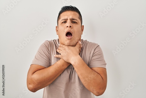 Hispanic young man standing over white background shouting and suffocate because painful strangle. health problem. asphyxiate and suicide concept.