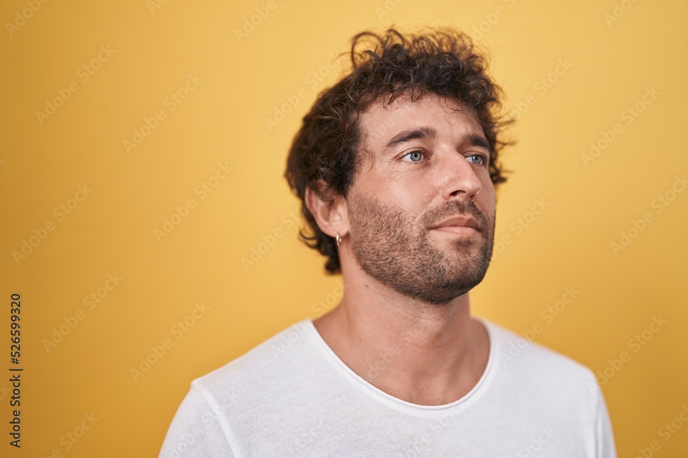 Young hispanic man standing looking to the side over isolated yellow background Young hispanic man standing looking to the side over isolated yellow background