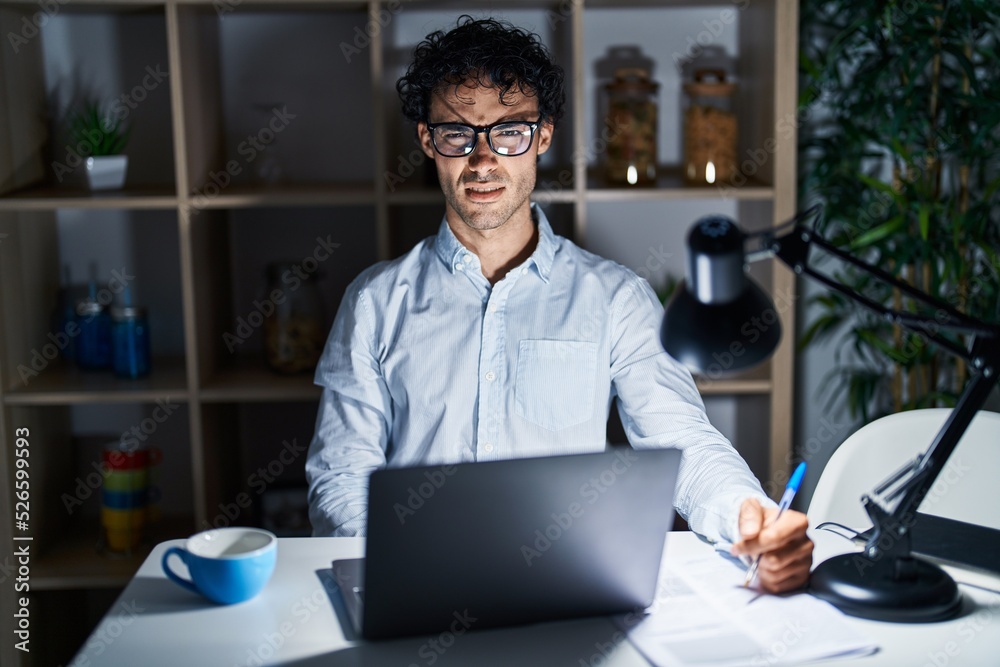 Hispanic man working at the office at night skeptic and nervous, frowning upset because of problem. negative person. Hispanic man working at the office at night skeptic and nervous, frowning upset because of problem. negative person.