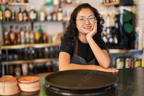 Fotografie Young chinese woman waitress smiling confident leaning on counter at restaurant