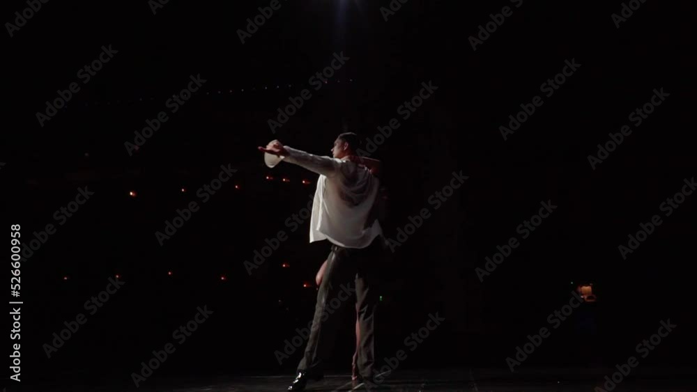 Dancing pair whirling in passionate tango or waltz,rear view,360 degree view from stage into dark auditorium.Monochrome footage of ballroom dancers performance,slightly illuminated by spotlights. Dancing pair whirling in passionate tango or waltz,rear view,360 degree view from stage into dark auditorium.Monochrome footage of ballroom dancers performance,slightly illuminated by spotlights.