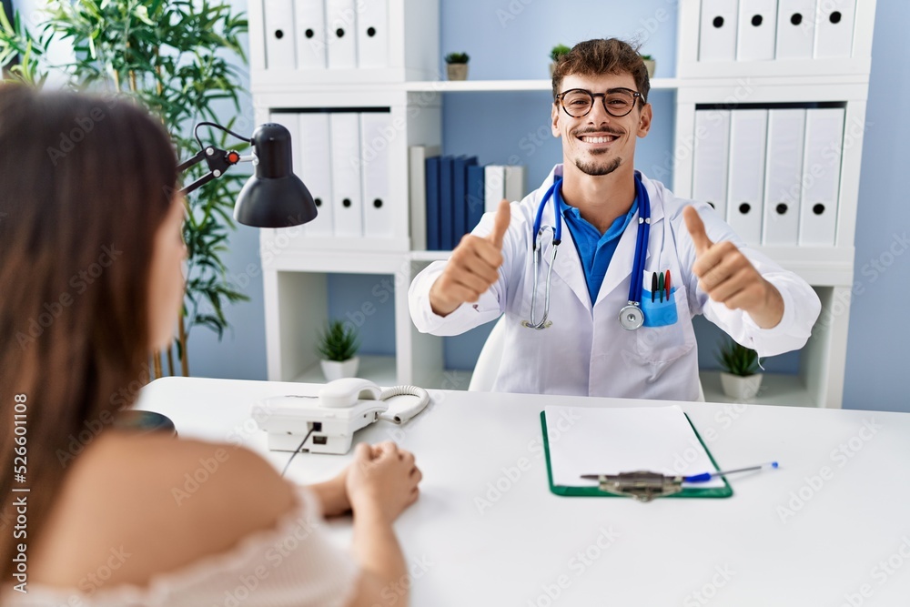 Young doctor with client at medical clinic approving doing positive gesture with hand, thumbs up smiling and happy for success. winner gesture. Young doctor with client at medical clinic approving doing positive gesture with hand, thumbs up smiling and happy for success. winner gesture.