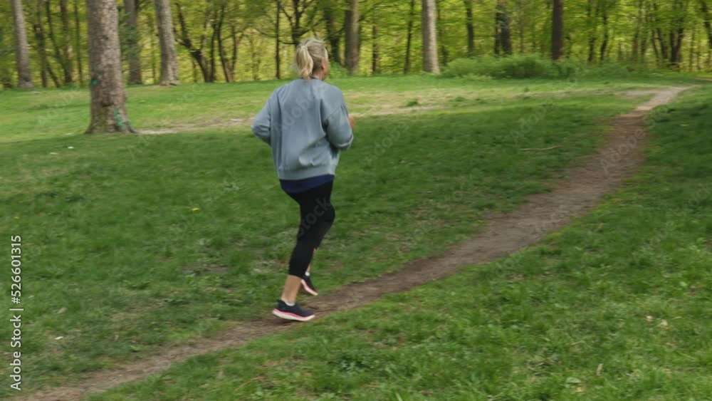 middle aged caucasian female jogging, training workout in green park nature. senior woman running cardio outdoors in summer. active retired grandmother doing sports. elderly woman wear grey sportswear middle aged caucasian female jogging, training workout in green park nature. senior woman running cardio outdoors in summer. active retired grandmother doing sports. elderly woman wear grey sportswear
