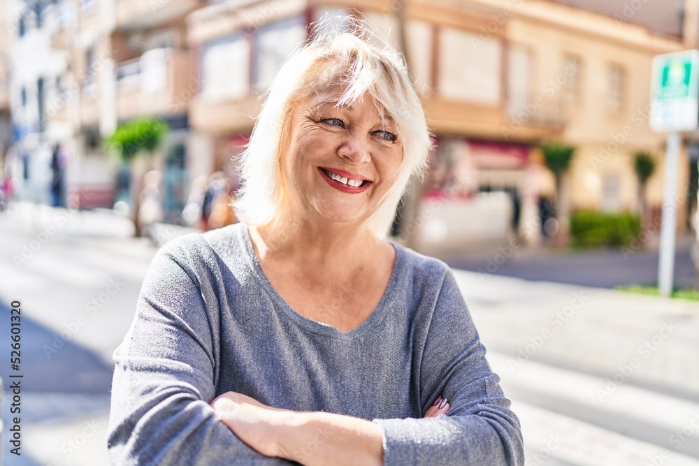 Middle age blonde woman smiling confident standing with arms crossed gesture at street Middle age blonde woman smiling confident standing with arms crossed gesture at street